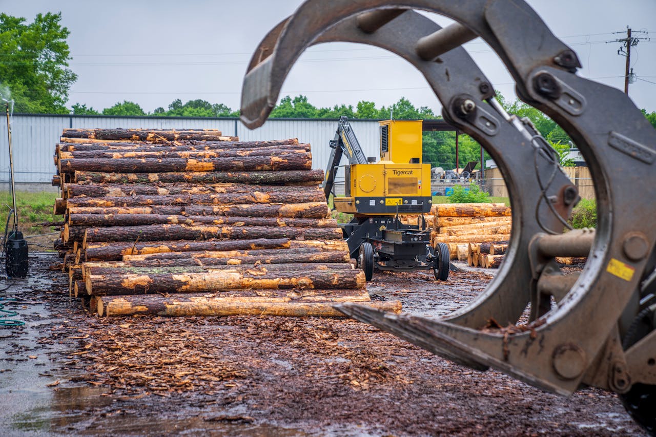 hero-img-01 Heavy machinery stacking timber logs at an industrial site amid a natural backdrop.