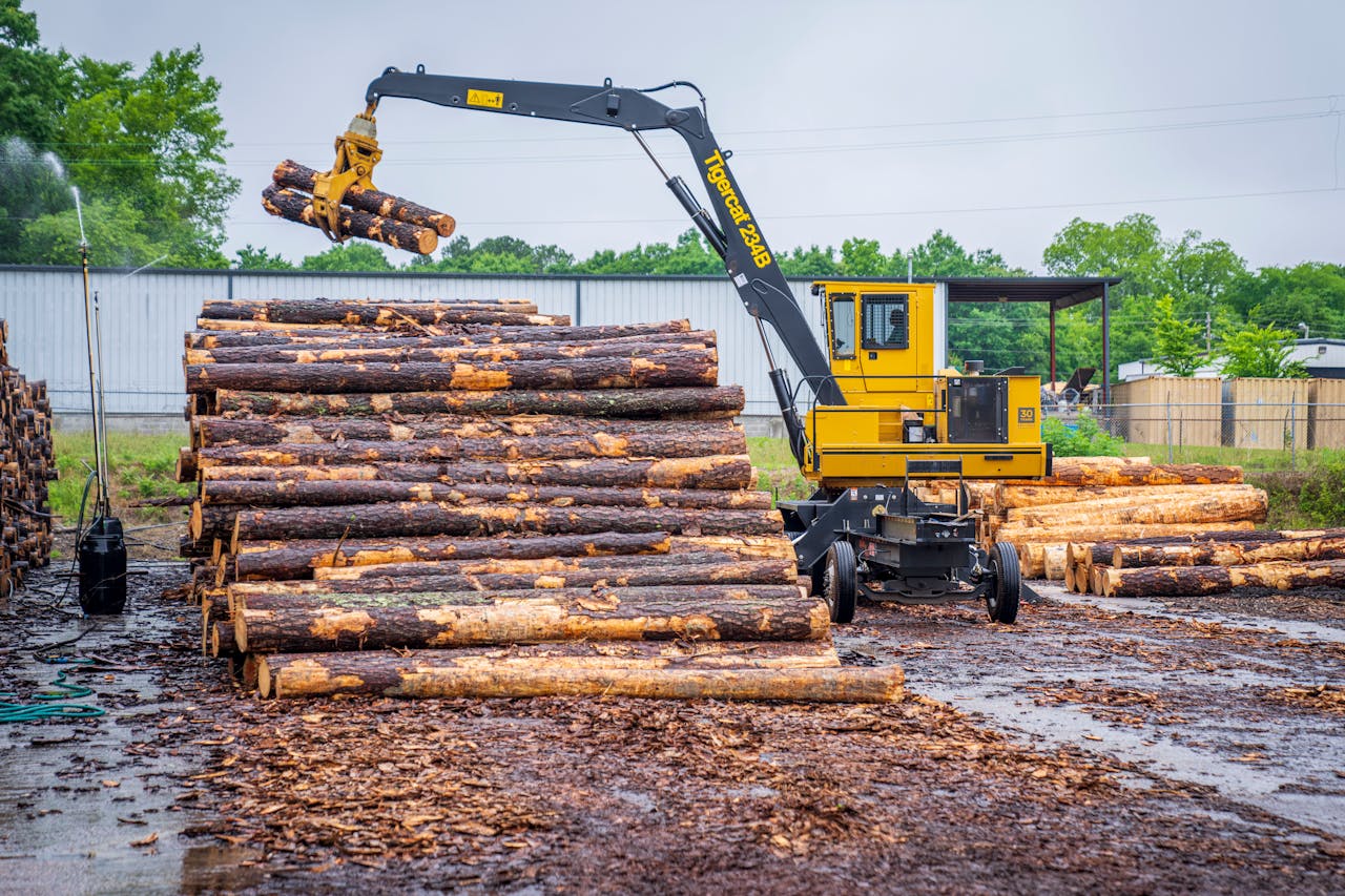 hero-img-02 Yellow material handler lifting logs at a lumber yard, showcasing modern industrial machinery in action.